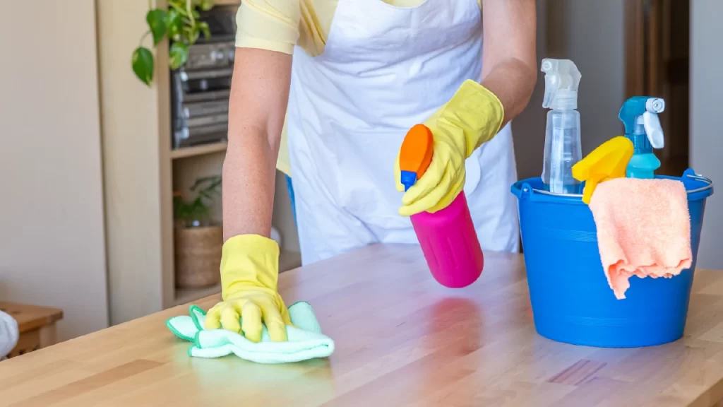 Home Cleaning Service Worker Using Spray Bottle And Bucket Of Cleaning Products For Efficient Dust And Germ Removal